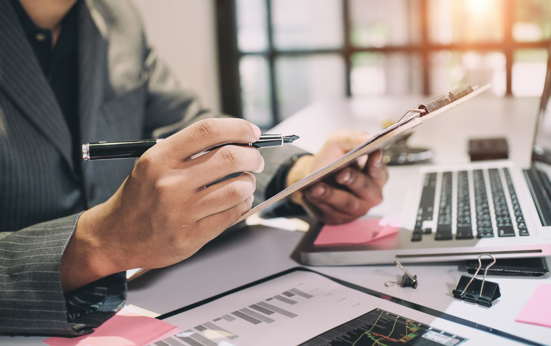 Man in a suit sits at a desk with a clipboard