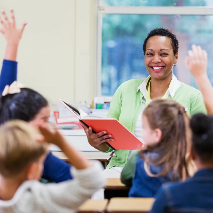 Teacher holding a workbook at the front of a primary school class